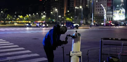 Juan Carlos Sánchez ajusta su telescopio mientras espera clientes que quieran ver la Luna a cambio de una contribución voluntaria durante un eclipse lunar parcial en Buenos Aires, Argentina, el 27 de agosto de 2026. (AP Foto/Natacha Pisarenko)