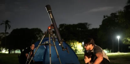 Hector García mira a la Luna a través de un telescopio y un celular adaptado con su hijo, durante un eclipse lunar parcial, en Caracas, Venezuela, el 27 de agosto de 2026. (AP Foto/Ariana Cubillos)