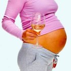 Mid section image of young pregnant woman holding a glass of champagne on white