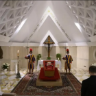 El Papa Francisco en su ataúd abierto, vestido con una túnica roja, la mitra papal en la cabeza y un rosario en la mano.
