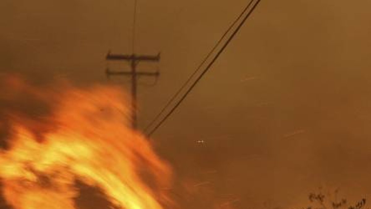 FILE - In this Nov. 9, 2018 file photo Wind-driven flames from a wildfire race up a slope and cross the road in Malibu, Calif. known as the Woolsey Fire, it has consumed tens of thousands of acres and destroyed multiple homes. Southern California Edison announced in its quarterly earnings report that its equipment probably caused the November 2018 Woolsey Fire that raged from north of Los Angeles through Malibu to the sea, killing three people and burning more than 1,600 homes and other buildings. (AP Photo/Reed Saxon,File)