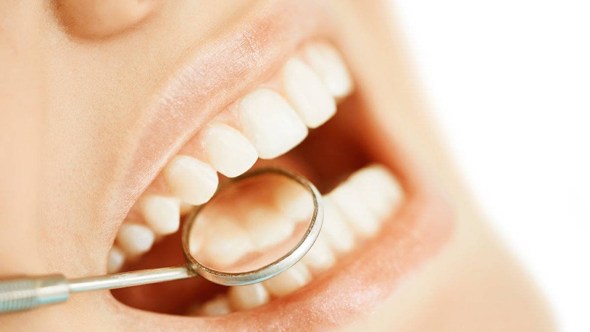 Dentist examining female teeth with angled mirror