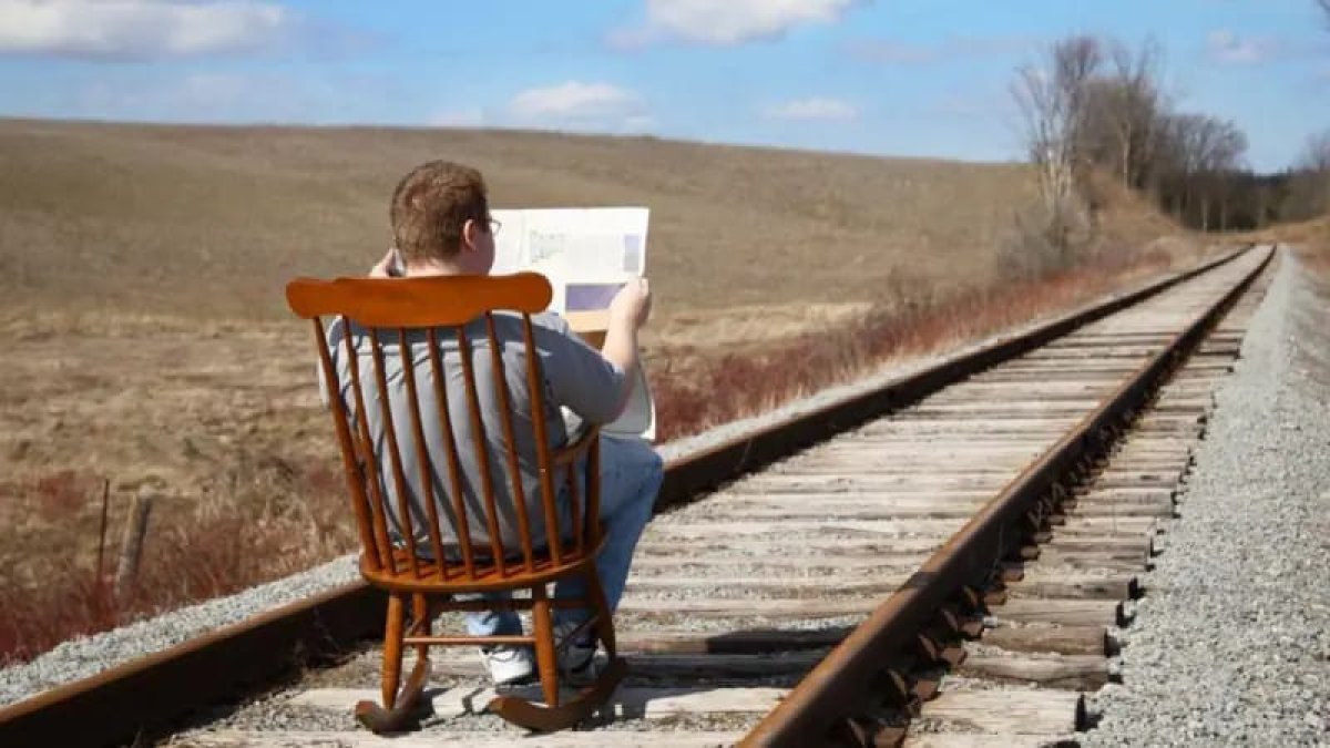 Sentido común, hombre lee periódico en tramo construido para que pase un tren. (Fuente externa).