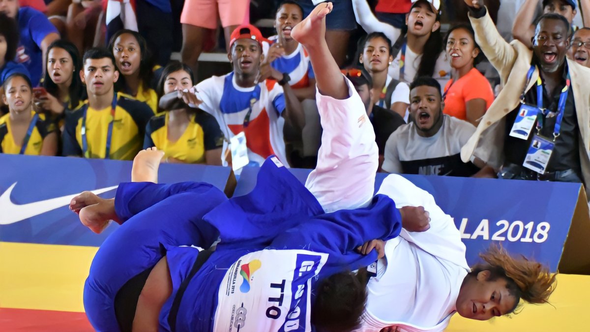 La dominicana Moira Morillo, uniforme blanco, sujeta fuerte a una rival de Trinidad y Tobago.