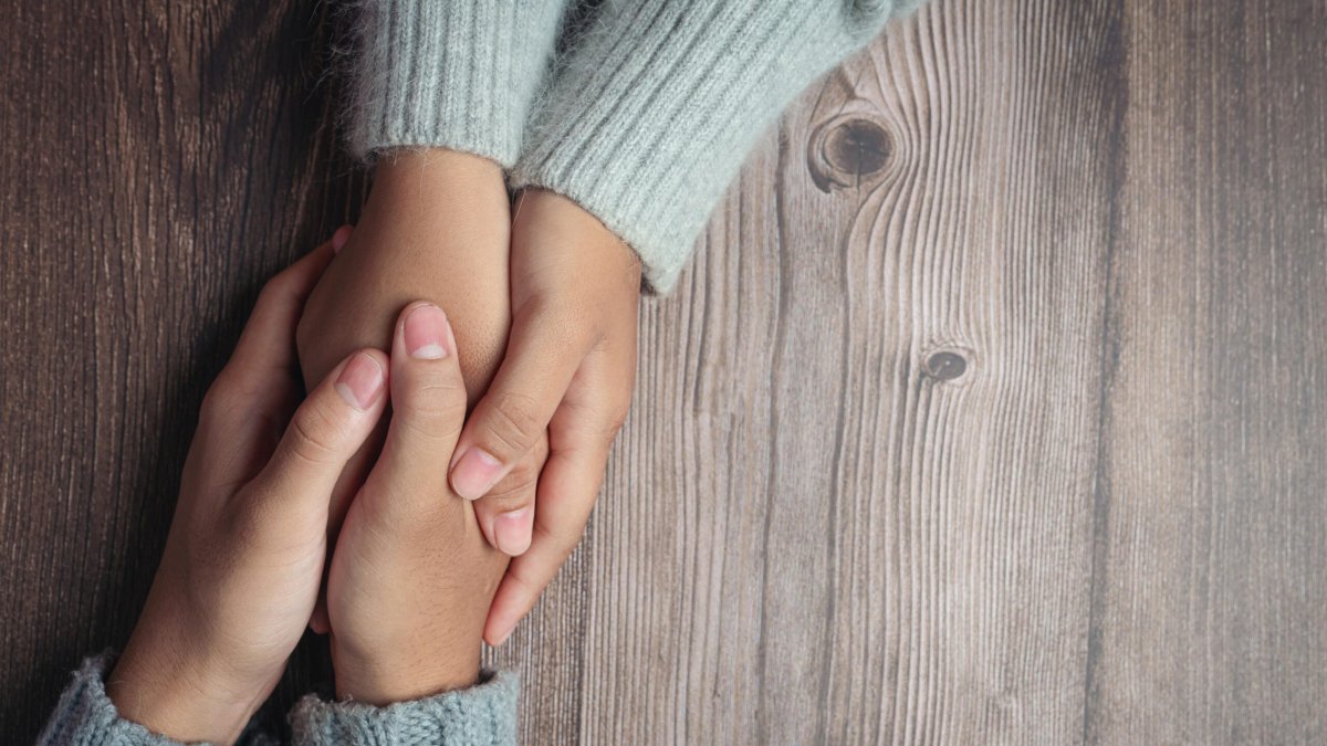 FEpVdGXkQQyEjRgpAlKc_two-people-holding-hands-together-with-love-and-warmth-on-wooden-table-min