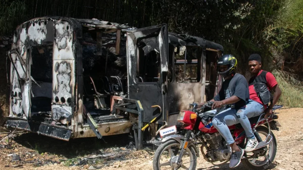 Personas en moto cruzan junto a un vehículo incinerado este lunes, en el sector de Kenscoff (Haití). EFE