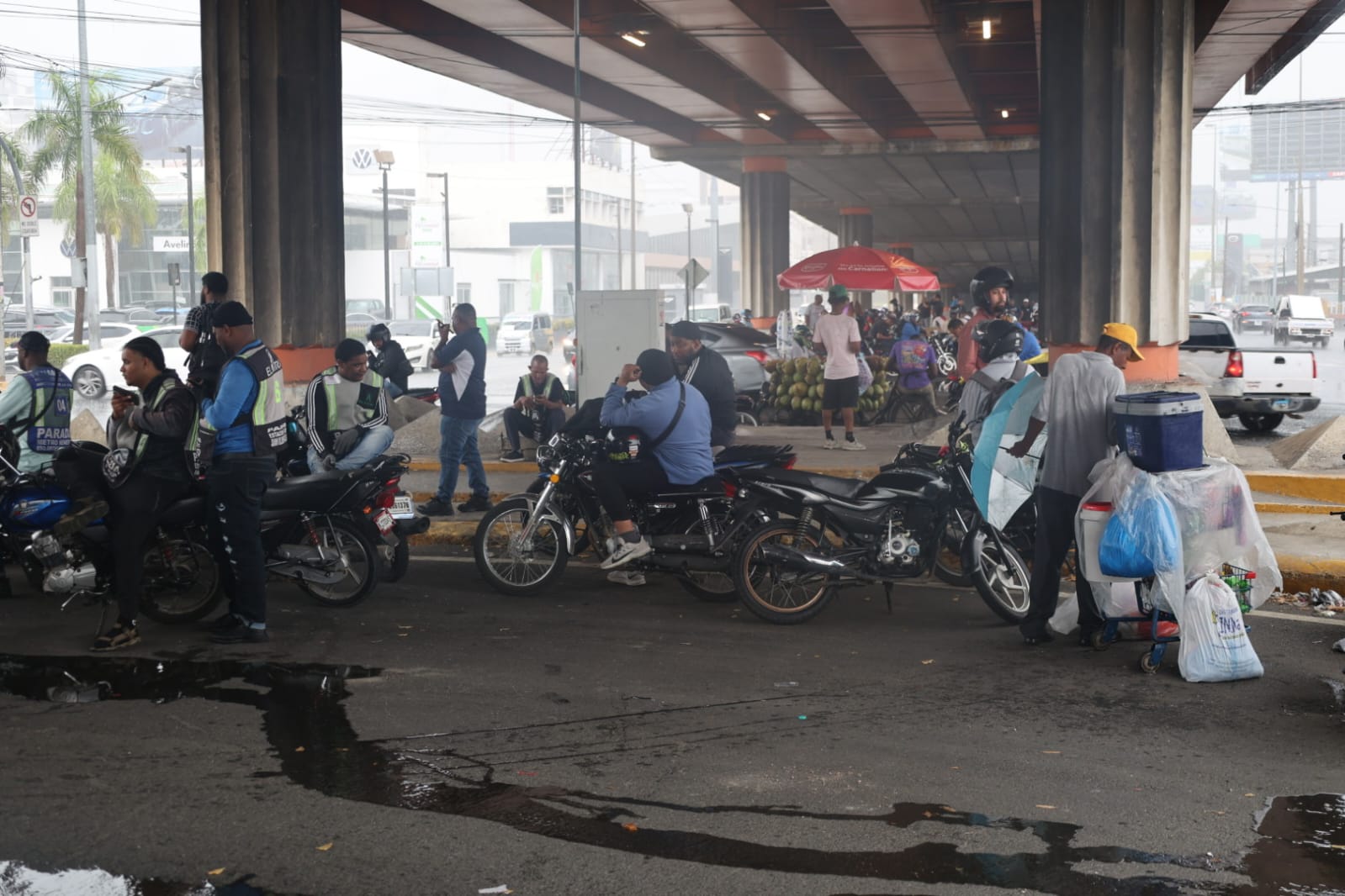 Motoristas y ciudadanos se resguardan de la lluvia bajo el elevado de la avenida John F. Kennedy durante los aguaceros registrados este sábado en Santo Domingo. Foto: Guillermo Burgos.
