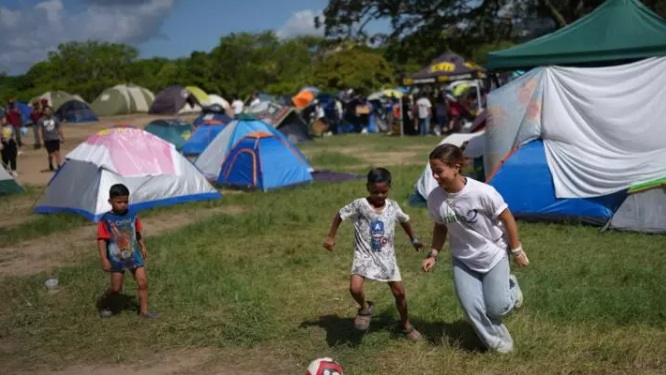 Una voluntaria juega al fútbol con niños en el Parque Generalísimo Francisco de Miranda, donde acampan personas cuyas viviendas resultaron dañadas por los terremotos, el miércoles 1 de julio de 2026. © AP/Matias Delacroix