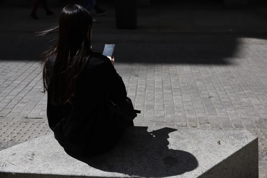 Una joven descansa sentada en un banco en la calle mientras mira su teléfono móvil. EFE/Mariscal