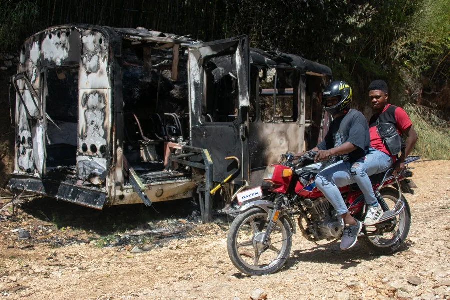 Personas en moto cruzan junto a un vehículo incinerado este lunes, en el sector de Kenscoff (Haití). EFE