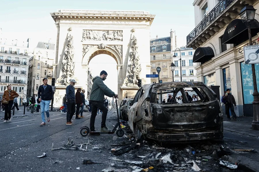 La gente pasa junto a un coche calcinado tras los enfrentamientos entre la policía antidisturbios y los manifestantes en París, Francia. EFE/EPA/MOHAMMED BADRA